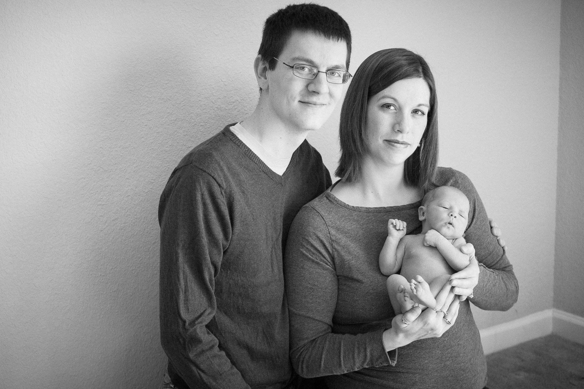 Two adults posing indoors, one holding a baby, in a black-and-white portrait in Pendleton.