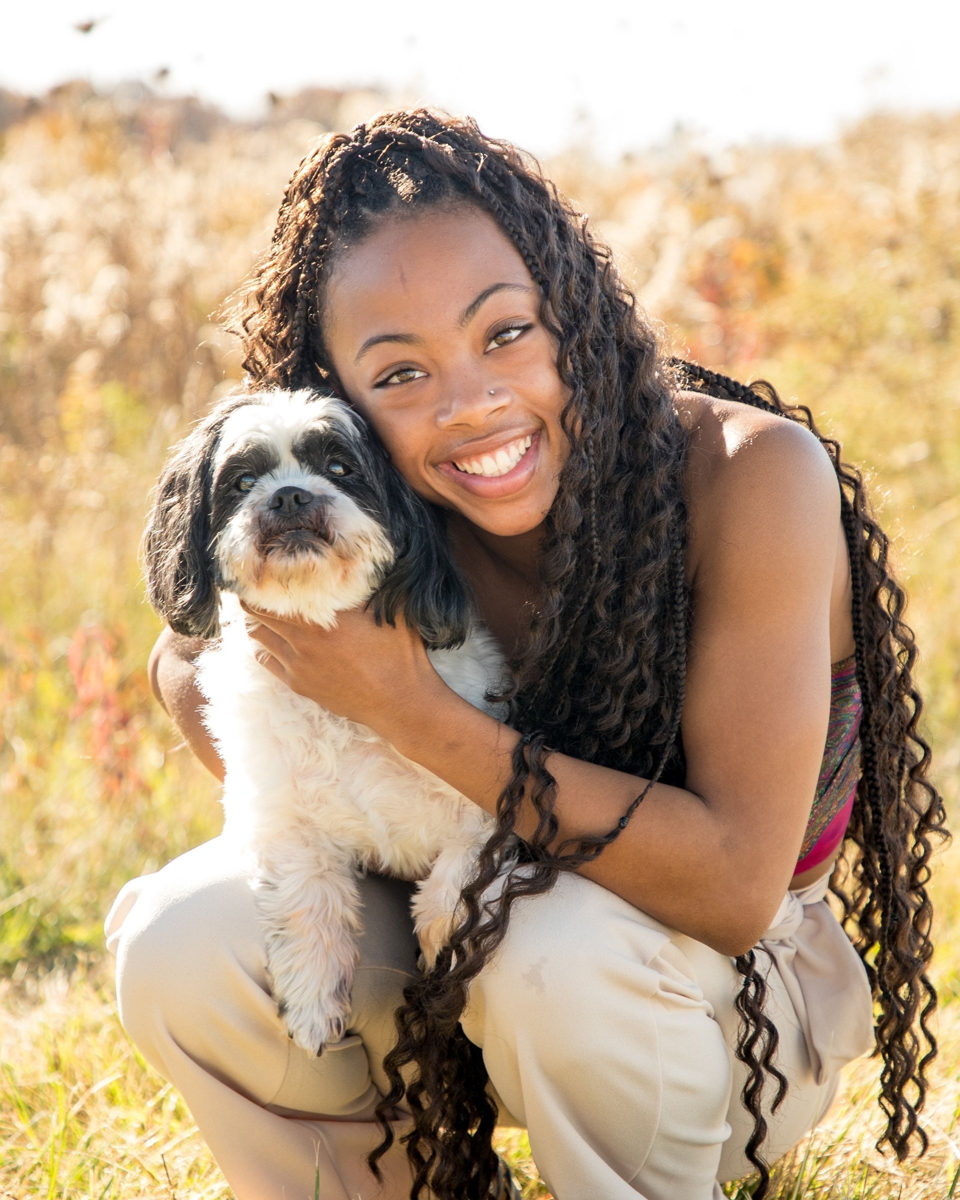 High school girl in Fishers Indiana smiling and hugging a black-and-white dog in a sunlit grassy field