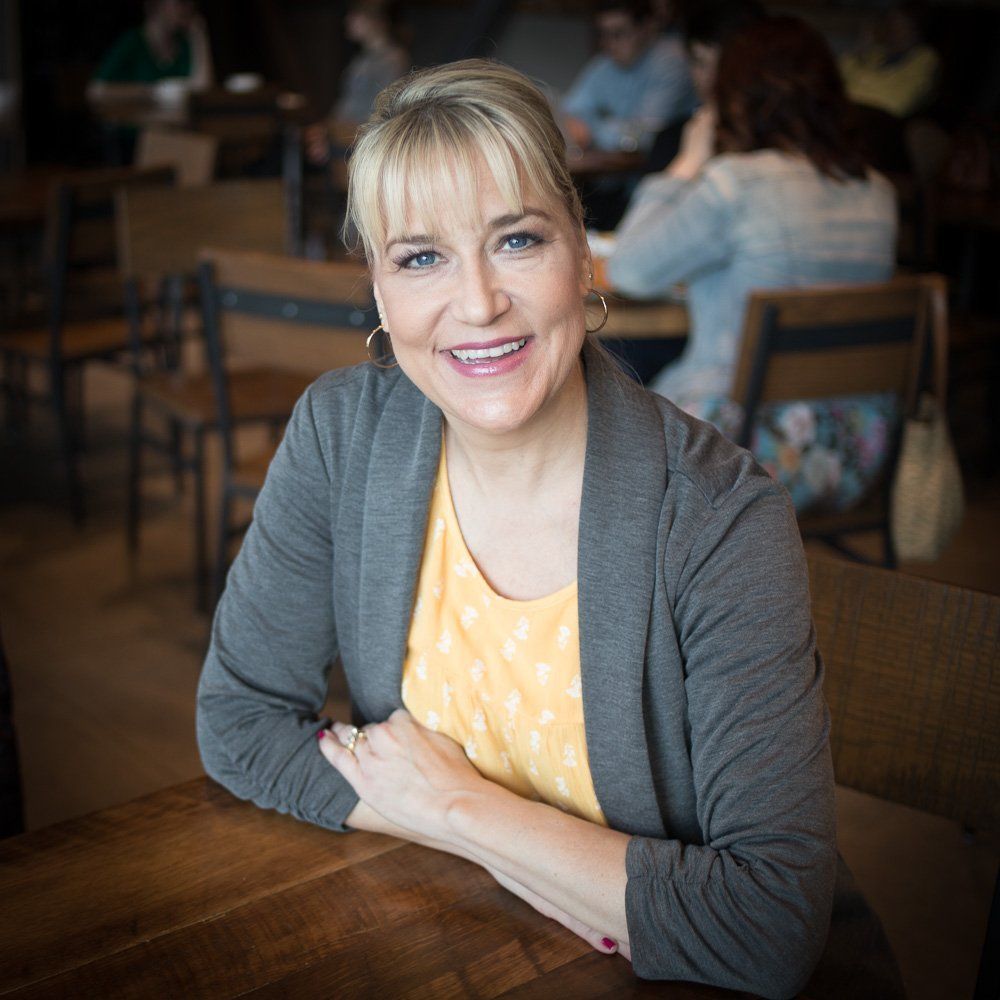Smiling woman in a gray cardigan sitting at a wooden table in a café