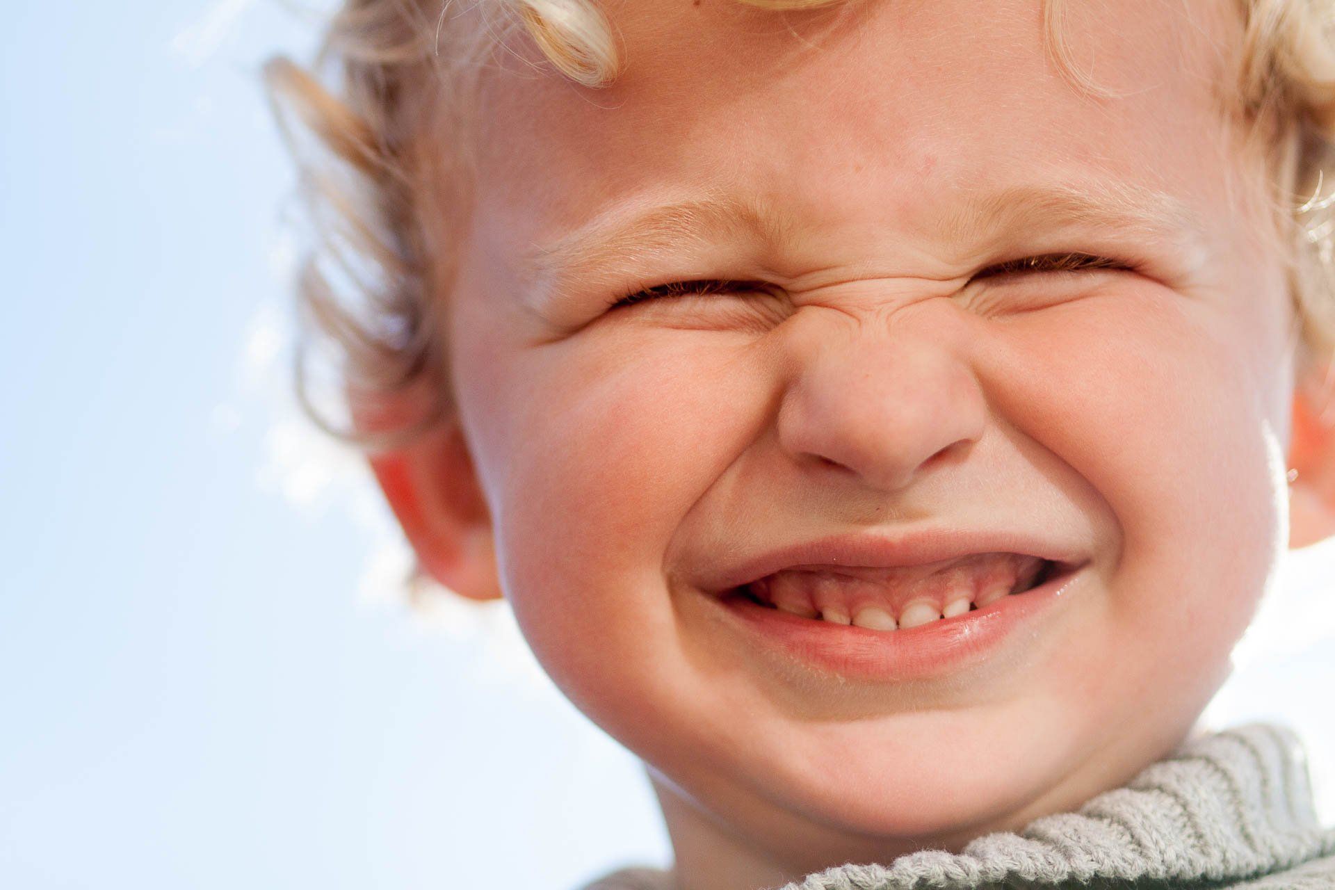 Close-up of a smiling child with eyes shut, against a bright sky background in Carmel, Indiana.