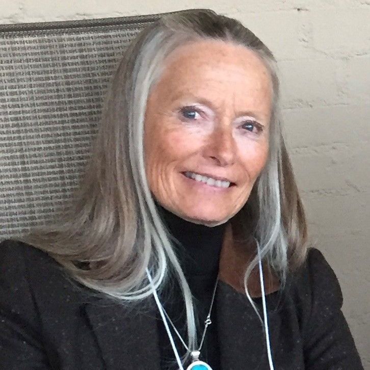 A woman with gray hair is smiling and wearing a necklace
