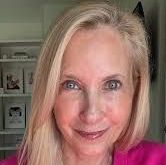A woman in a suit and pearl necklace is smiling for the camera.