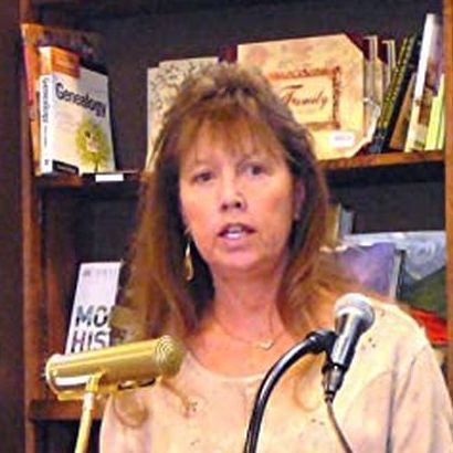 A woman is speaking into a microphone in front of a bookshelf.