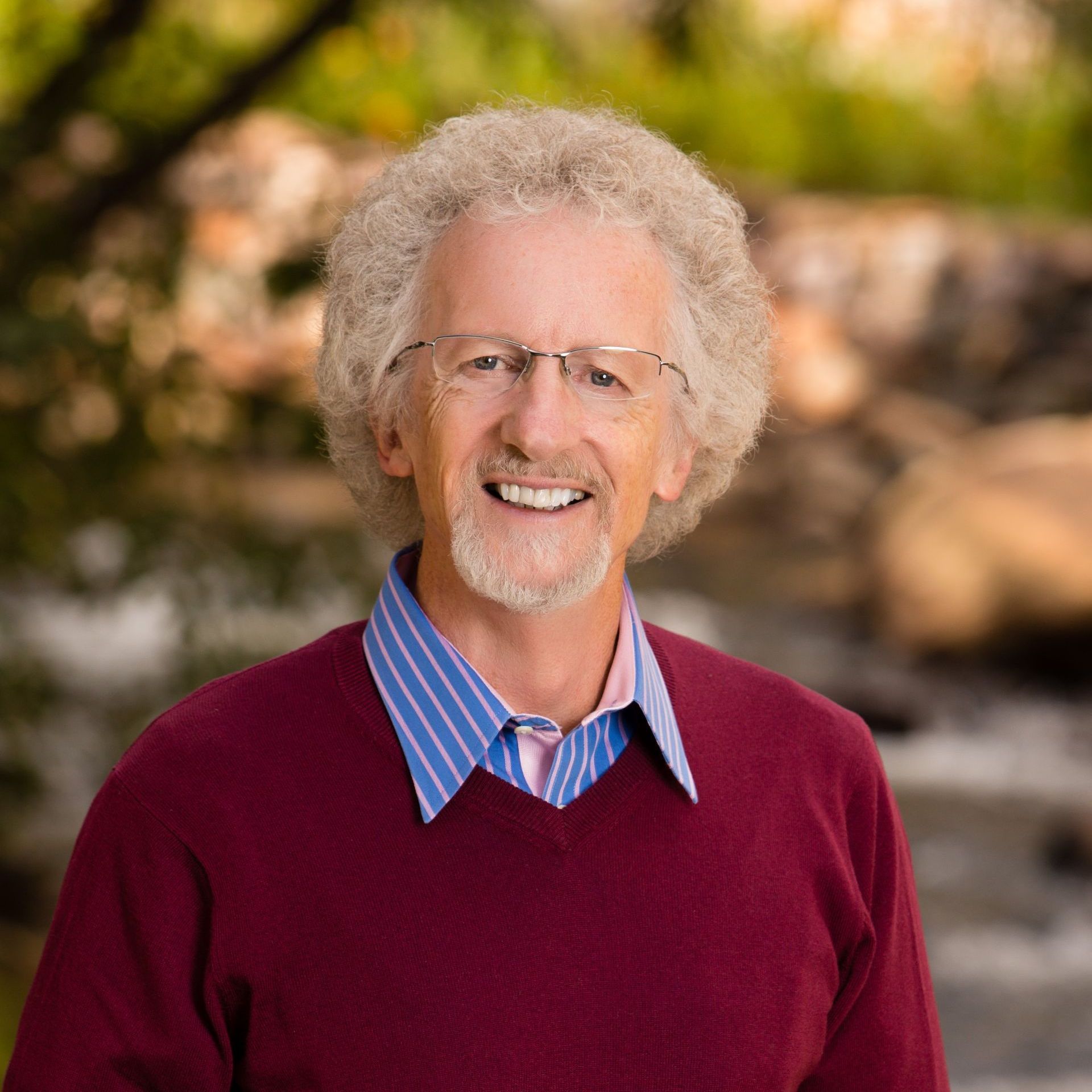 A man wearing glasses and a red sweater smiles for the camera