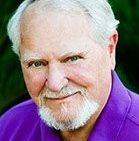 A man with a beard is wearing a purple shirt and smiling.