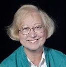 A woman wearing glasses and a blue sweater is smiling for the camera.