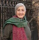 A woman wearing a green and red scarf is standing in front of a fence.