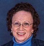 A woman wearing glasses and a blue turtleneck is smiling for the camera.