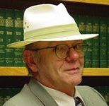 A man wearing a hat and glasses is standing in front of a bookshelf.