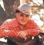 A man wearing a cowboy hat and a red shirt is sitting under a tree.