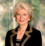 An older woman wearing a black jacket and earrings is smiling for the camera.