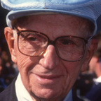 A man wearing glasses and a hat is smiling for the camera.