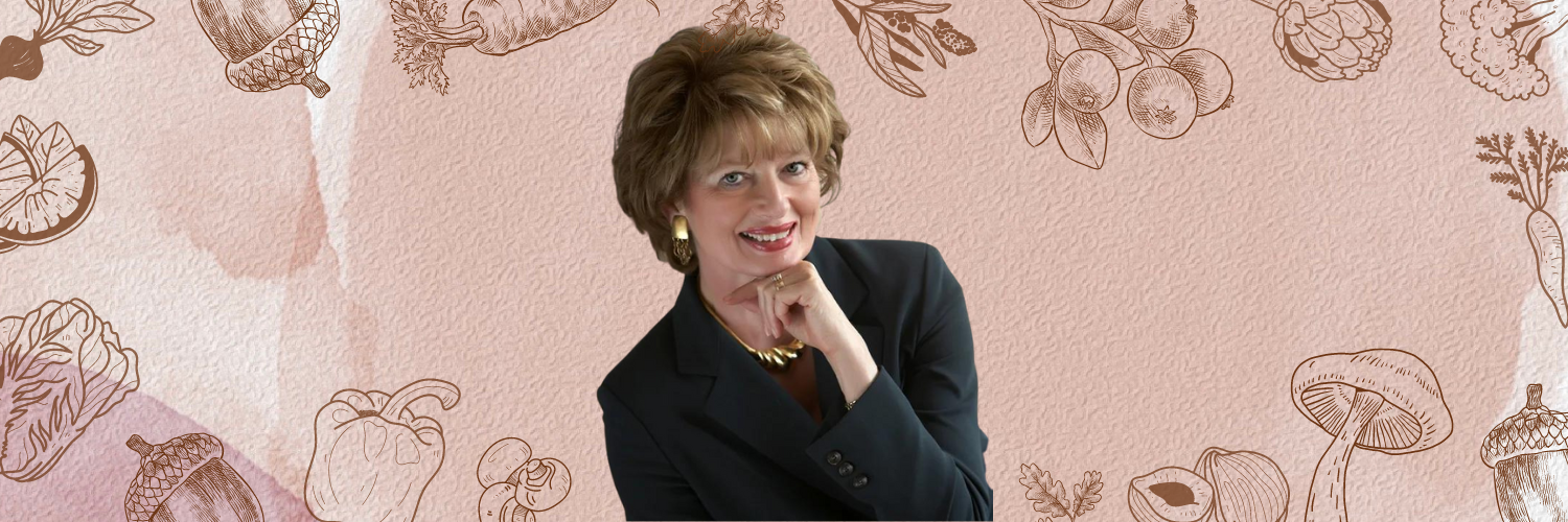 A woman in a suit is smiling with her hand on her chin