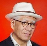 A man wearing a hat and glasses is standing in front of a red background.