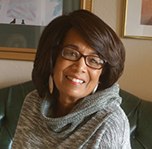 A woman wearing glasses and a scarf is sitting on a couch.
