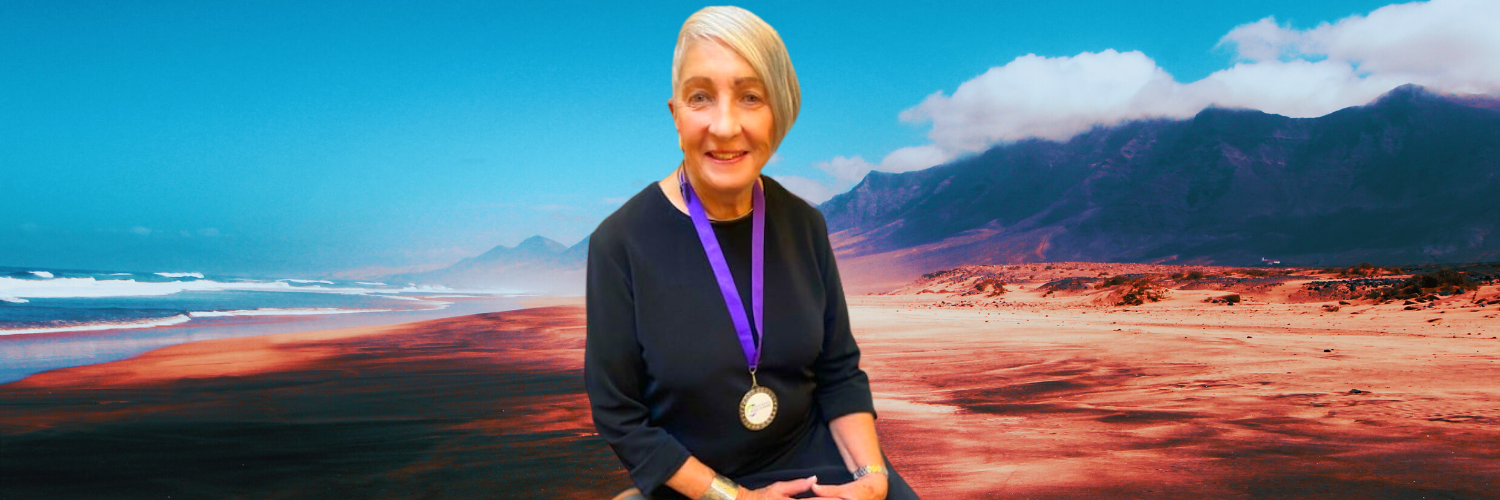 A woman with a medal around her neck is sitting on a beach.