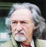 A man with long hair and a beard is wearing a green jacket.