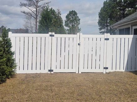 A white vinyl privacy fence with double gates in a suburban backyard.