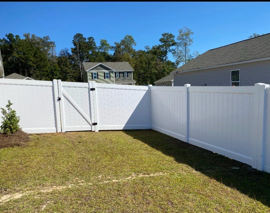 A white vinyl privacy fence with an attached gate borders a grassy backyard on a sunny day.