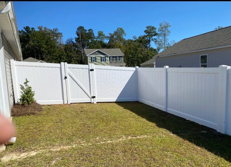 A bright white vinyl privacy fence encloses a small grassy backyard on a sunny day.