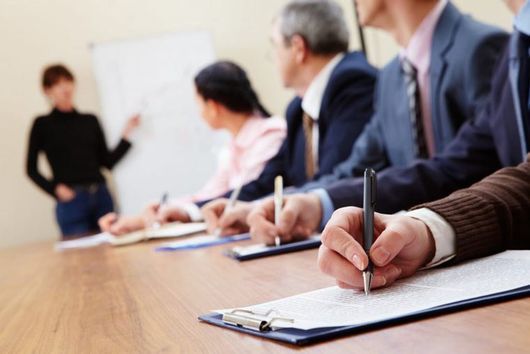 Riunione di lavoro con persone che prendono appunti mentre un relatore presenta alla lavagna.