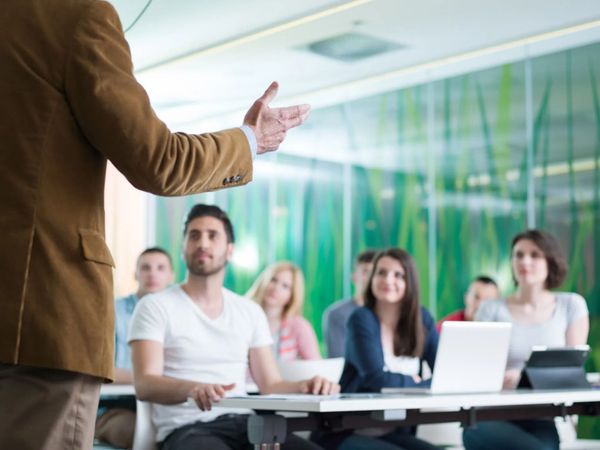 Il relatore si rivolge a un pubblico seduto in una sala conferenze con computer portatili e uno sfondo verde.