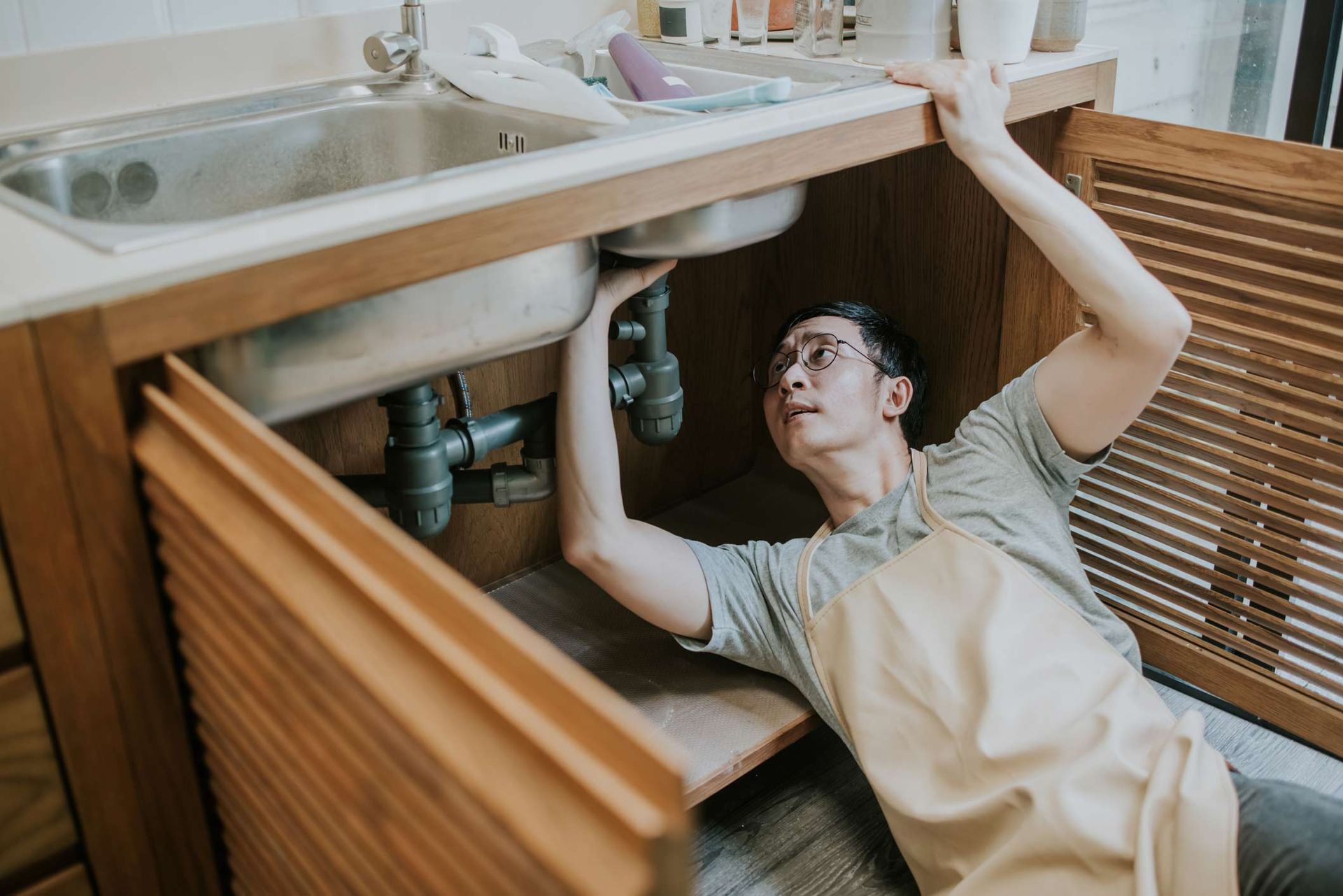 A Man Is Fixing A Sink In A Kitchen — Rome, GA — Crider Plumbing Co A Man Is Fixing A Sink In A Kitchen — Rome, GA — Crider Plumbing Co
