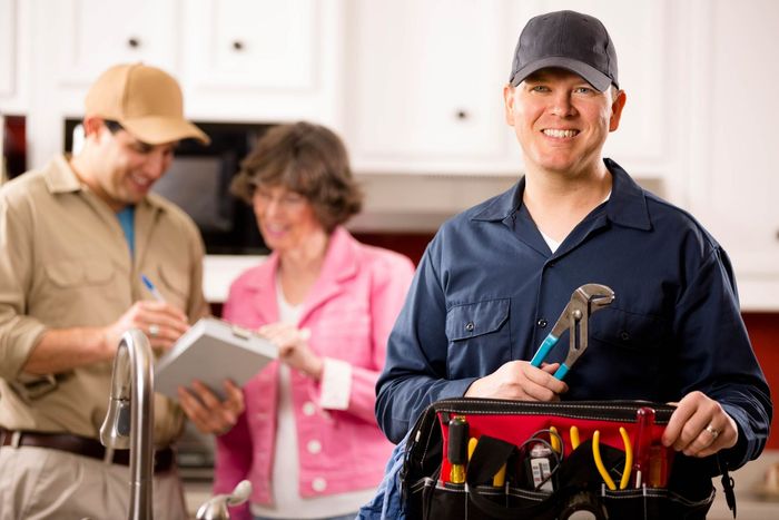 A Plumber Is Holding A Toolbox And Smiling In Front Of A Couple — Rome, GA — Crider Plumbing Co A Plumber Is Holding A Toolbox And Smiling In Front Of A Couple — Rome, GA — Crider Plumbing Co
