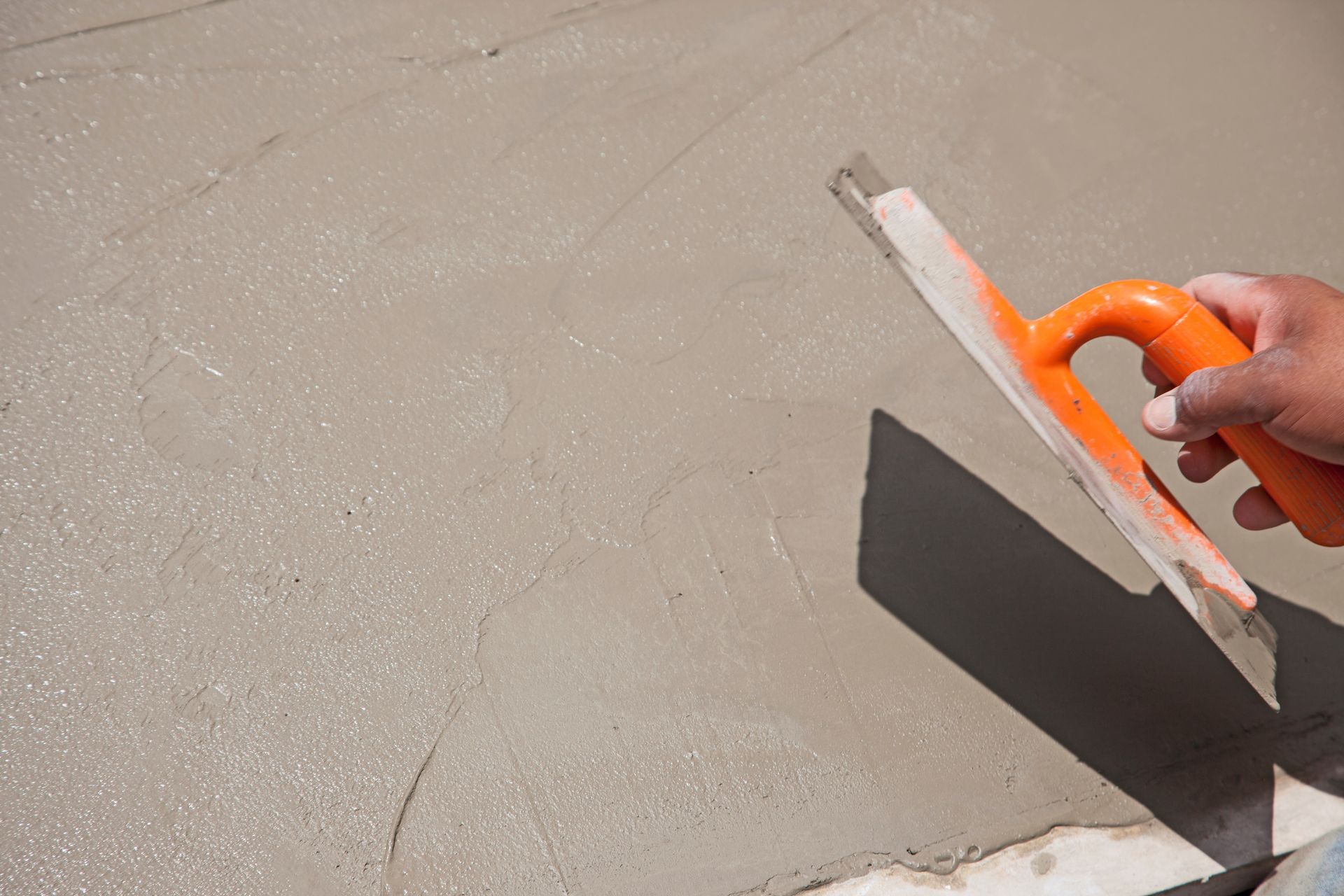 A contractor applying cement to a driveway installation using a trowel.