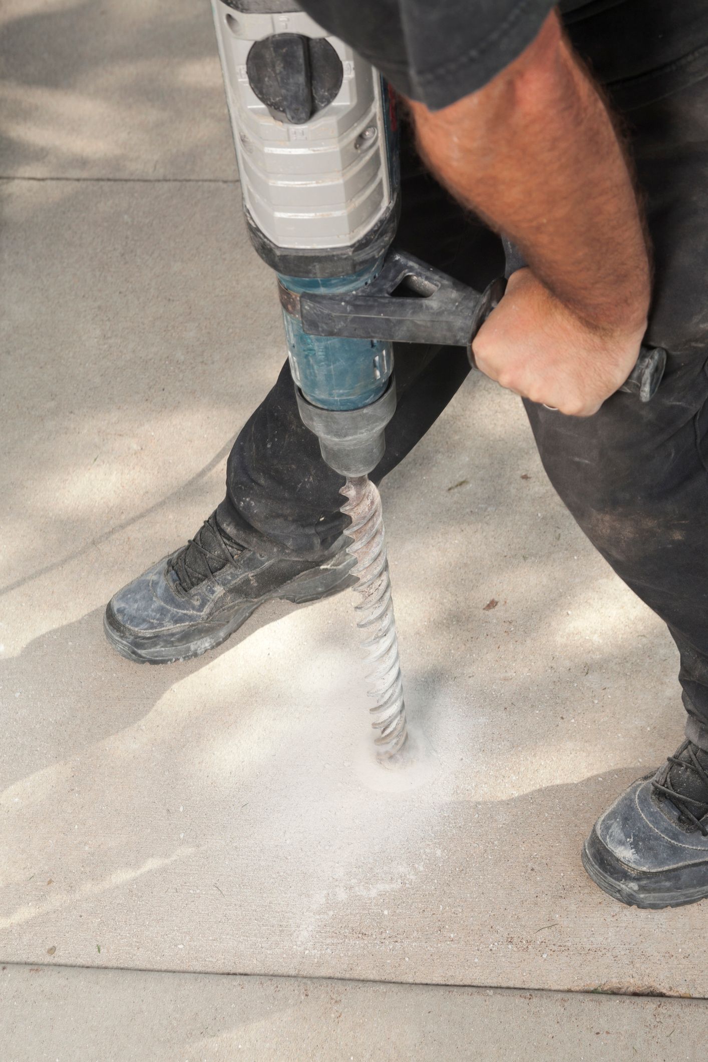 A worker is drilling a hole in the concrete driveway with a hammer drill tool for mudjacking.