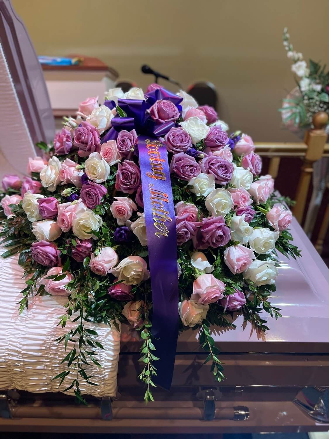Pink and purple floral funeral spray atop a casket with a blue ribbon