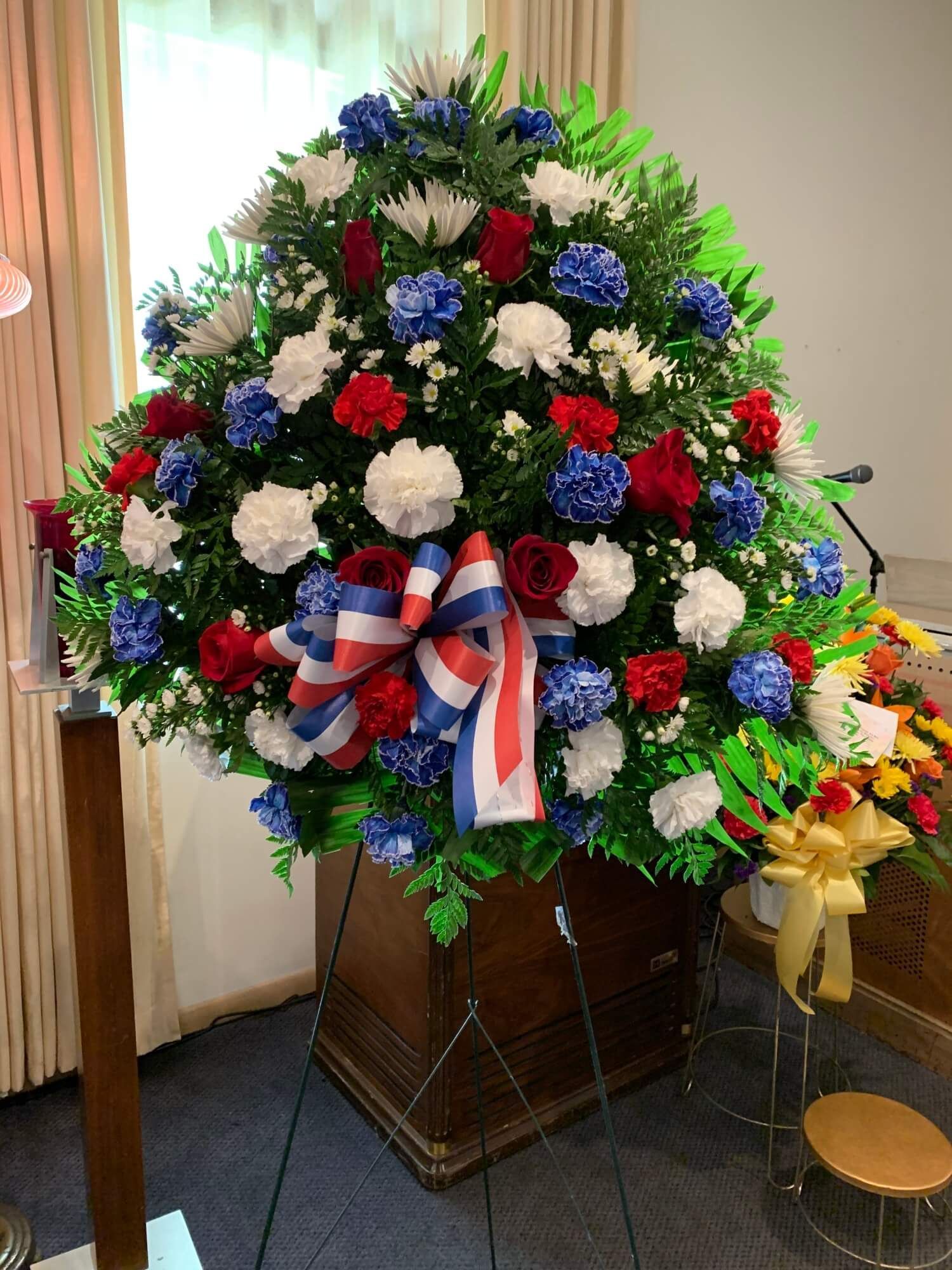 Red, white, and blue floral wreath on an easel with a patriotic bow in an indoor setting