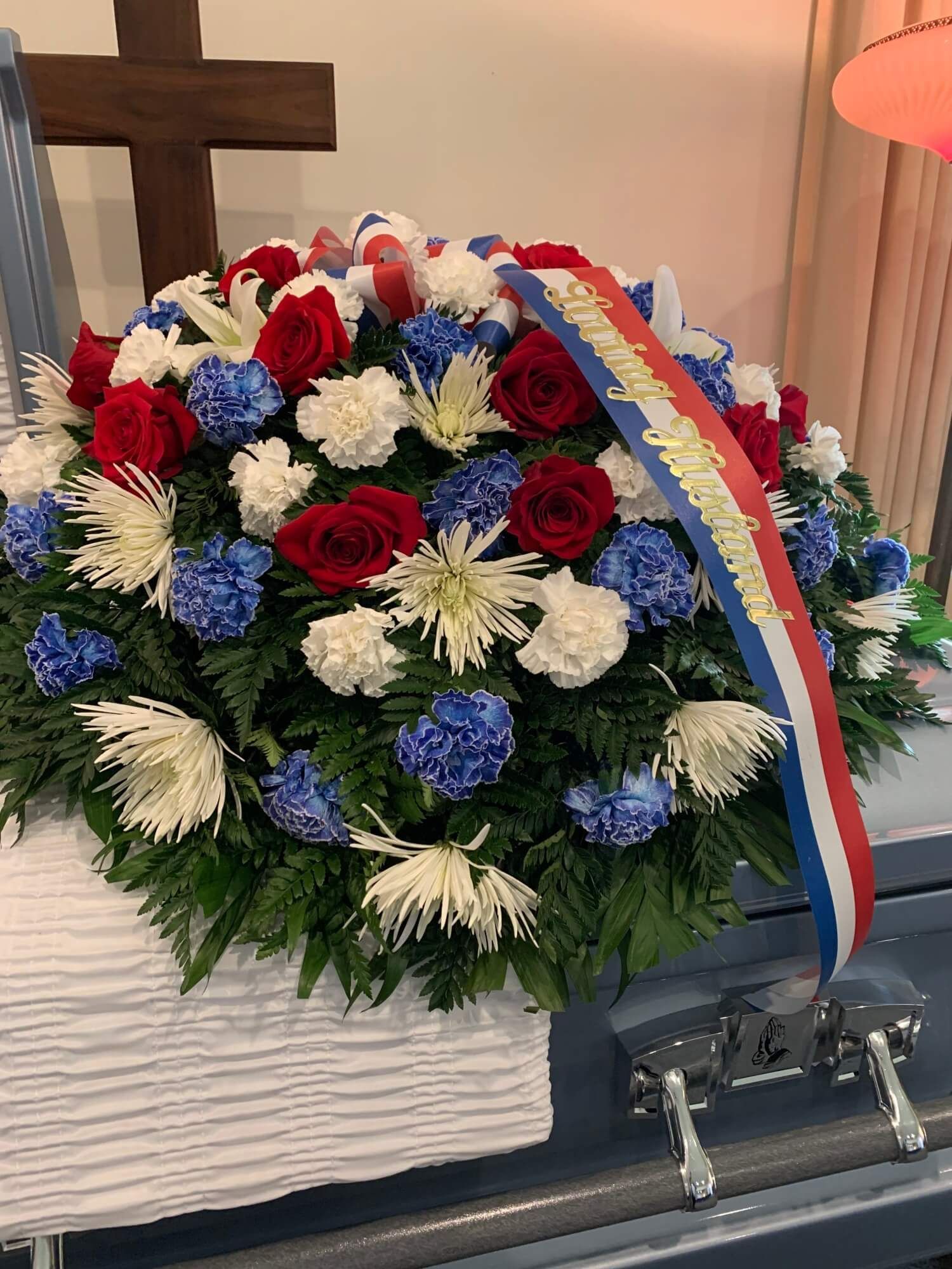Floral funeral wreath of red, white, and blue flowers with ribbon on a casket