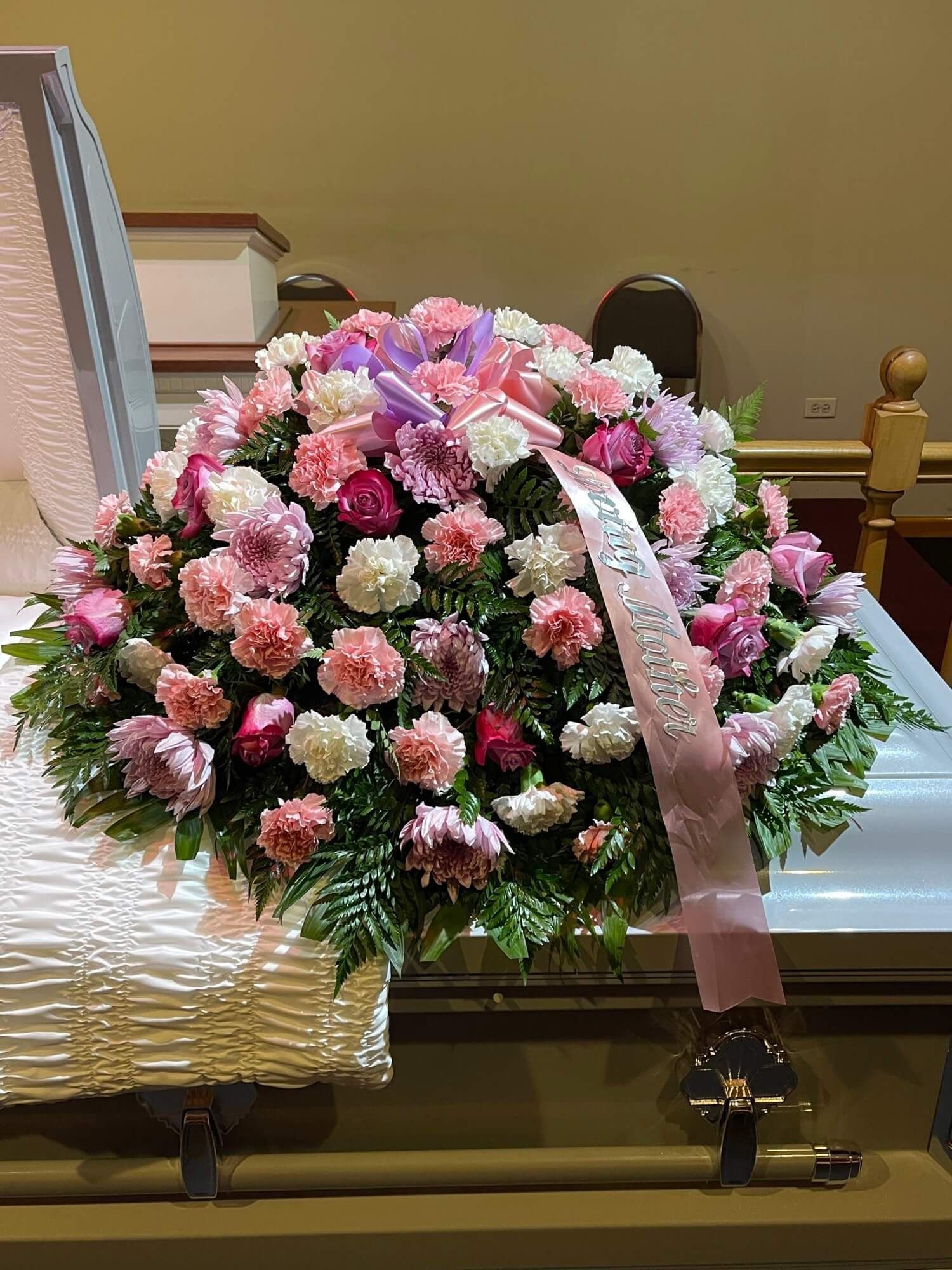 Pink and white floral funeral spray with ribbon on a casket in a chapel
