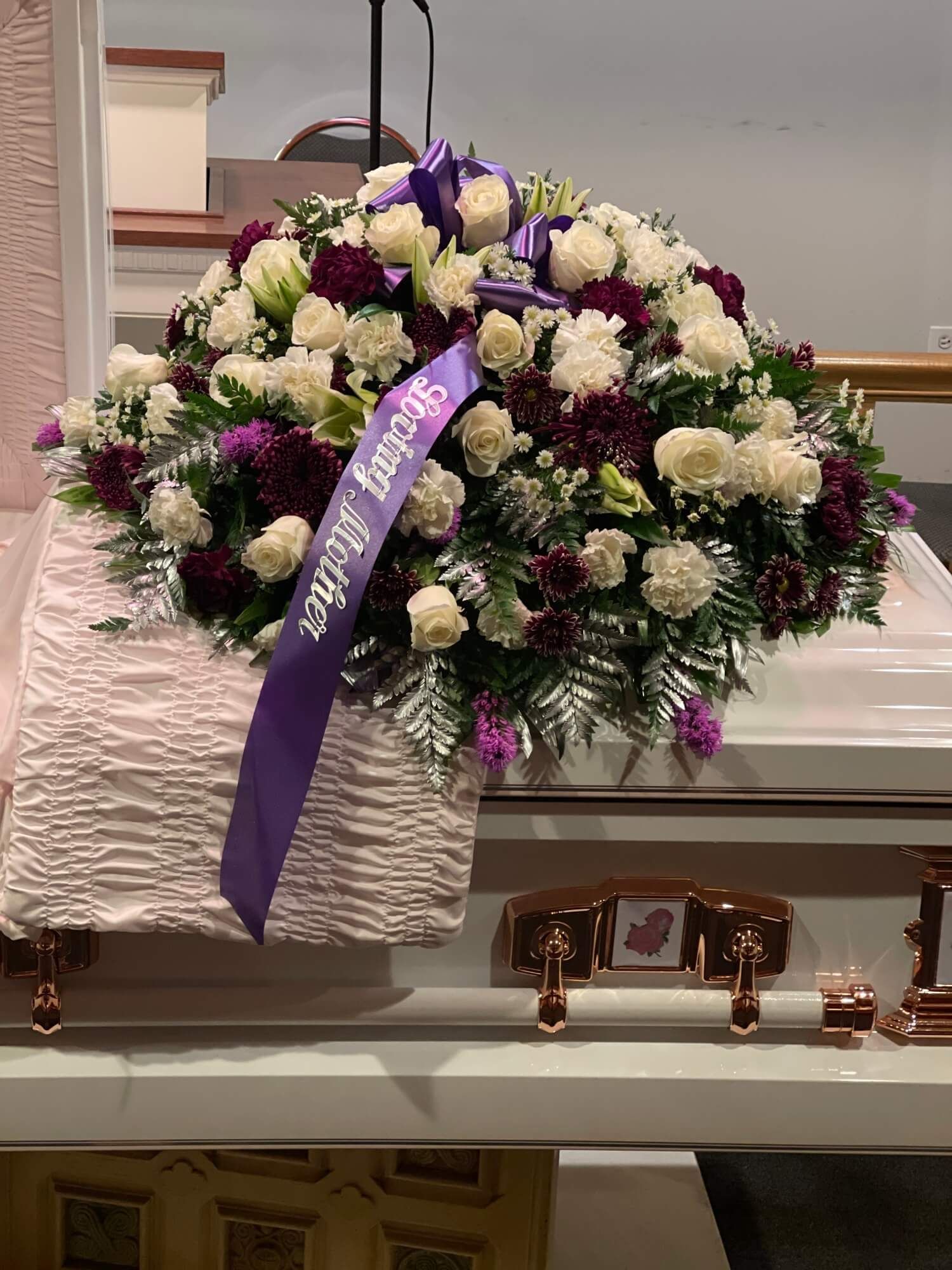 Floral funeral casket spray with white, purple, and burgundy flowers on a white casket