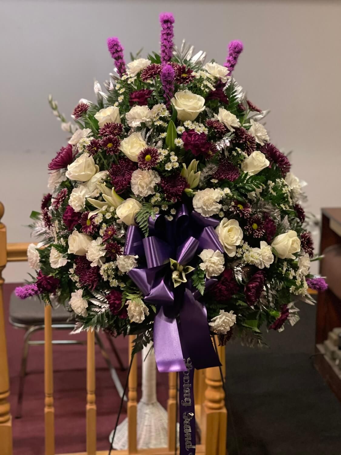 Purple and white funeral wreath on an easel with a large purple ribbon