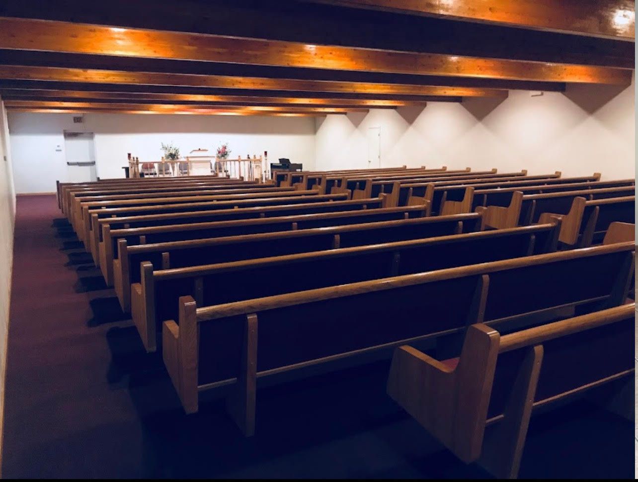 Empty church pews facing a small altar in a wood-beamed chapel.