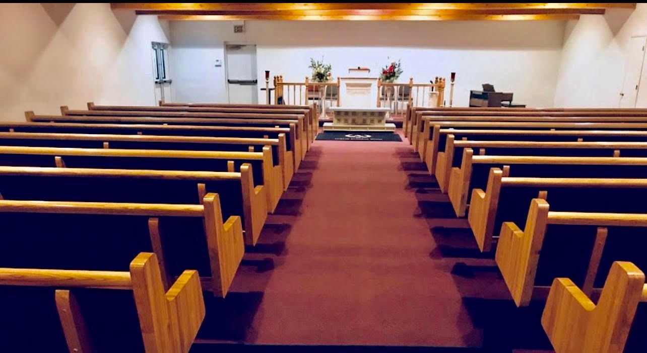 Empty church sanctuary with wooden pews, red carpet aisle, and altar at the front