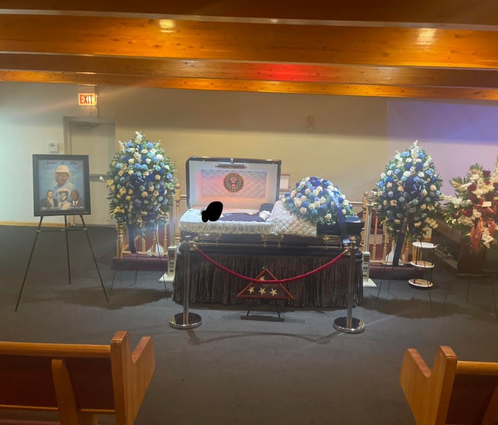 Memorial altar with framed portrait, white and blue flower arrangements, and candles in a banquet hall