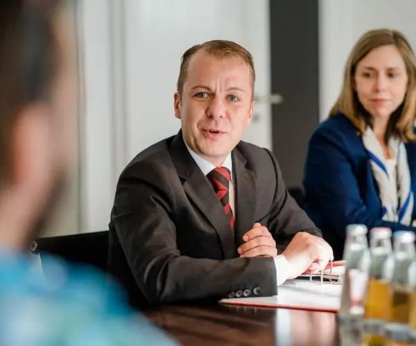 Geschäftstreffen mit zwei Personen an einem Konferenztisch, eine Person spricht, während die andere zuhört.