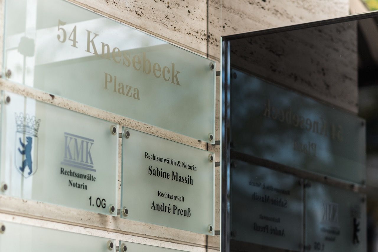 Glasige Bürowegweiser am Gebäudeeingang, darunter „54 k…“ und Namen in schwarzer Schrift