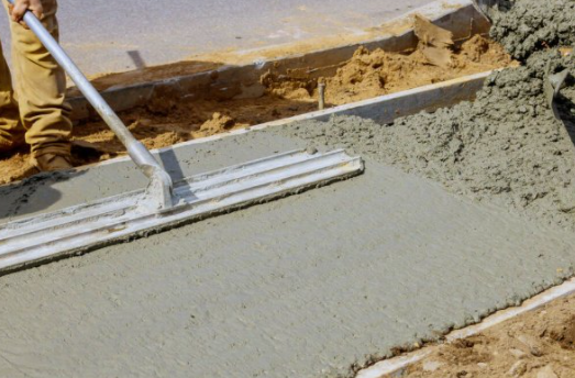 Concrete poured in sidewalk frame and worker leveling concrete.