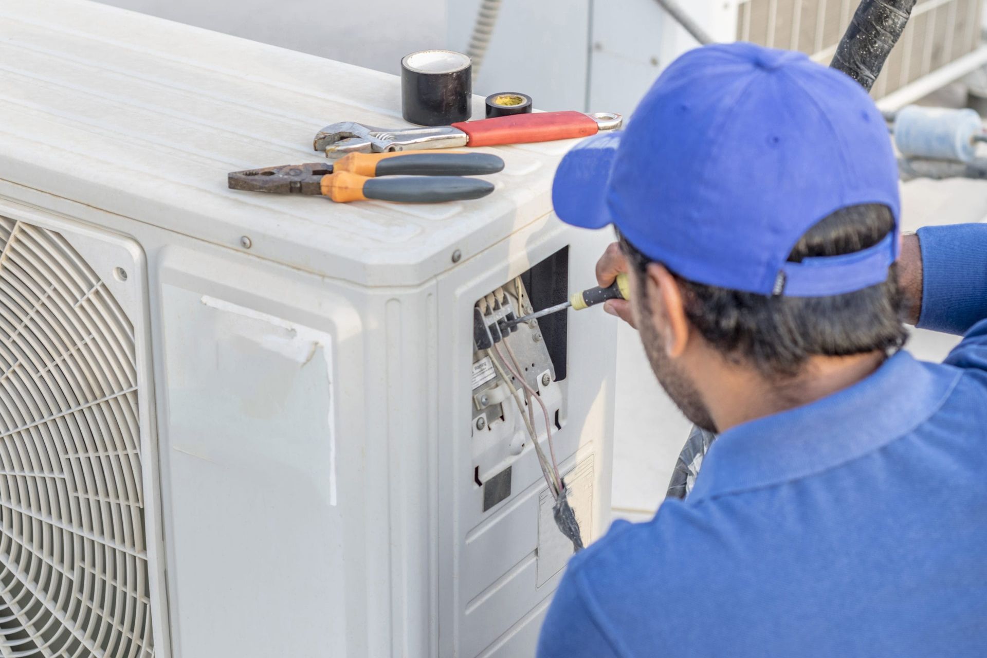 Technician repairing an outdoor air conditioner unit with tools on top.