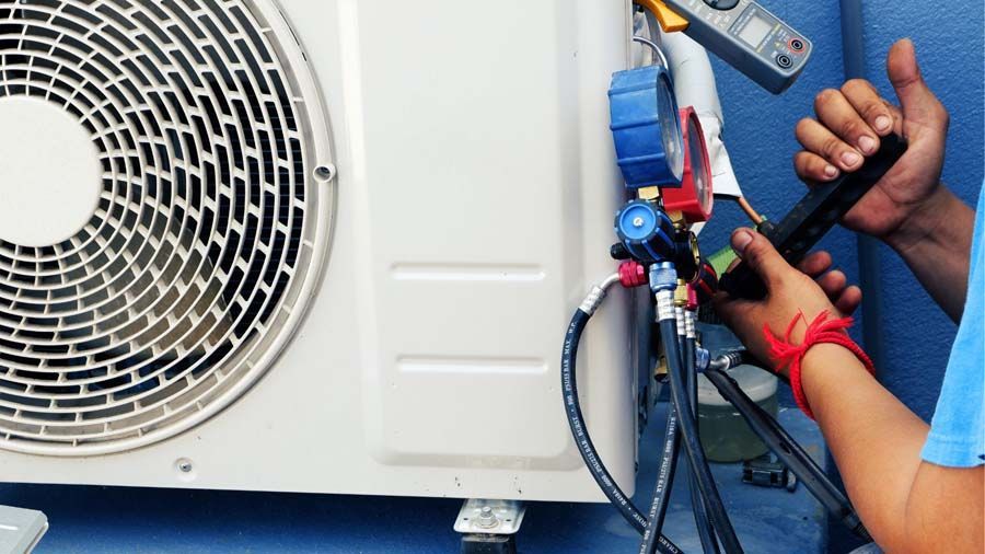 Technician servicing an outdoor air conditioner unit with gauges and hoses connected