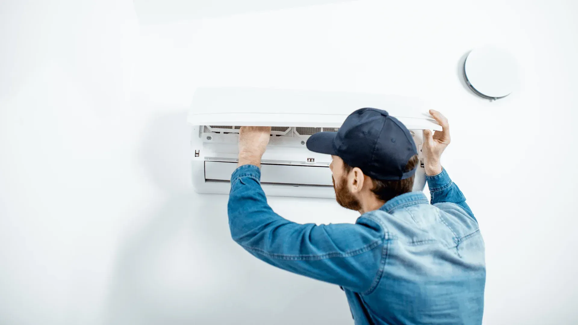 Technician installing a wall-mounted air conditioner on a white wall