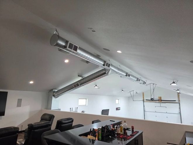 Modern lounge with black chairs, a table, and exposed silver ductwork under a slanted ceiling.