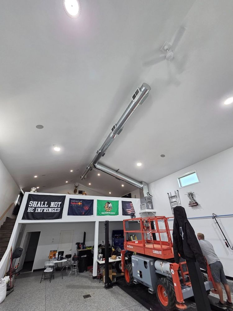 Bright garage interior with a red scissor lift, ceiling lights, and wall art above a workbench.