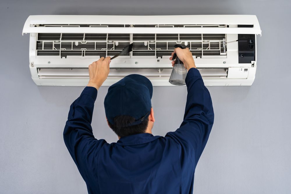 Technician cleaning the filters of a wall-mounted air conditioner with a spray bottle