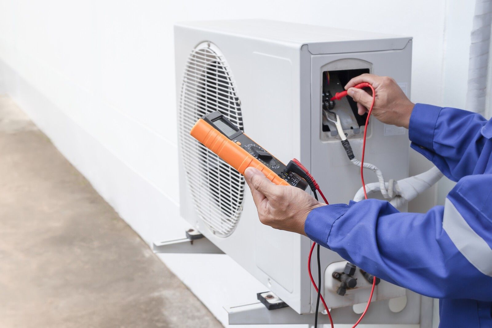 Technician testing an outdoor air conditioner unit with a multimeter and probe leads