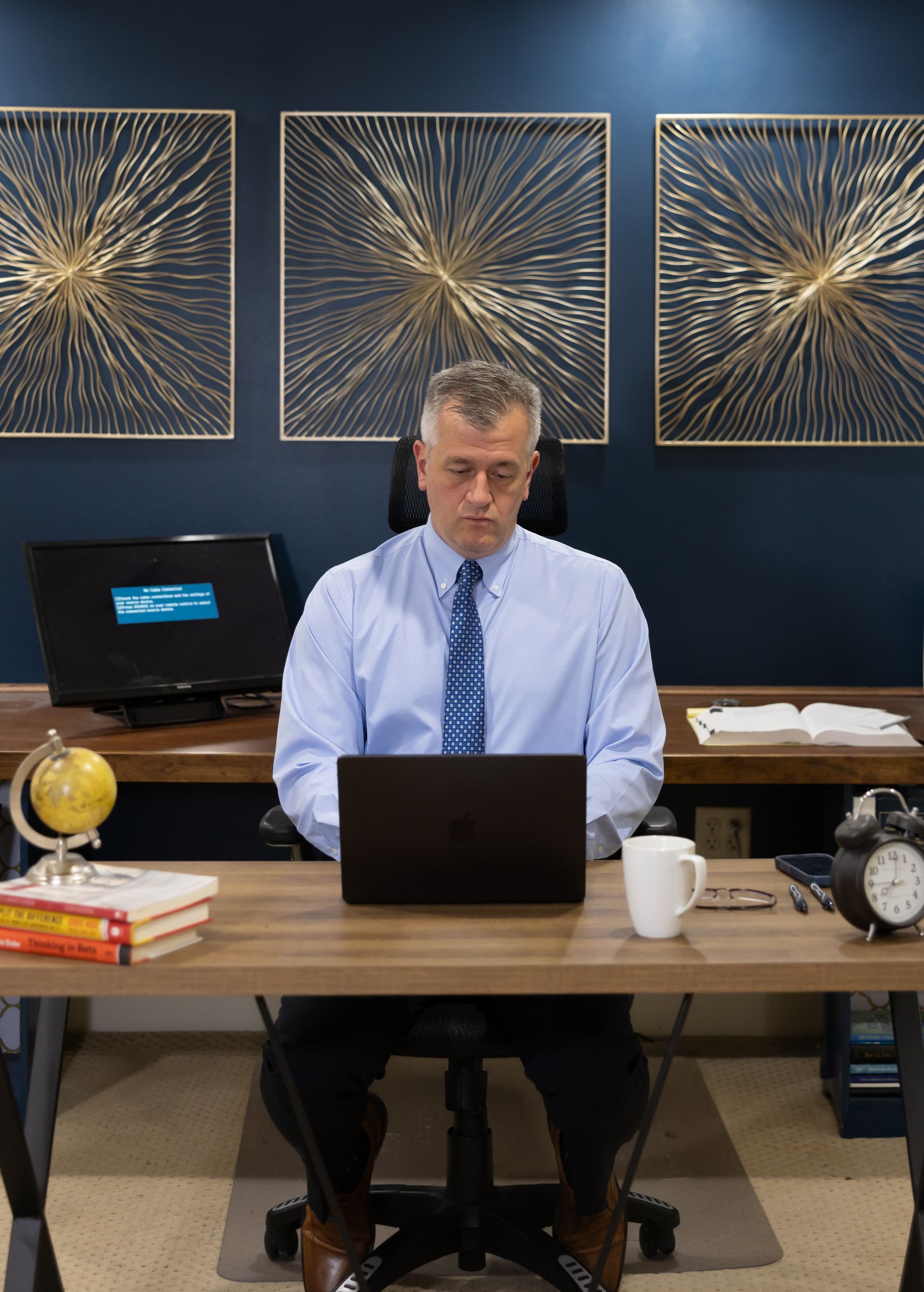 Man in blue shirt and tie working at a desk with laptop in an office setting